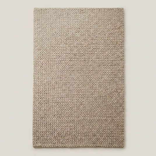 Translation missing: es.Chunky braided knit rug in neutral beige with thick textured yarn, ideal for cozy Nordic interiors and warm minimalist spaces