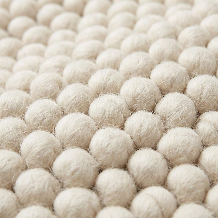 Translation missing: es.Close-up of chunky wool rug texture showing thick looped fibers and dense handmade weave in soft ivory tone, highlighting craftsmanship and premium material quality