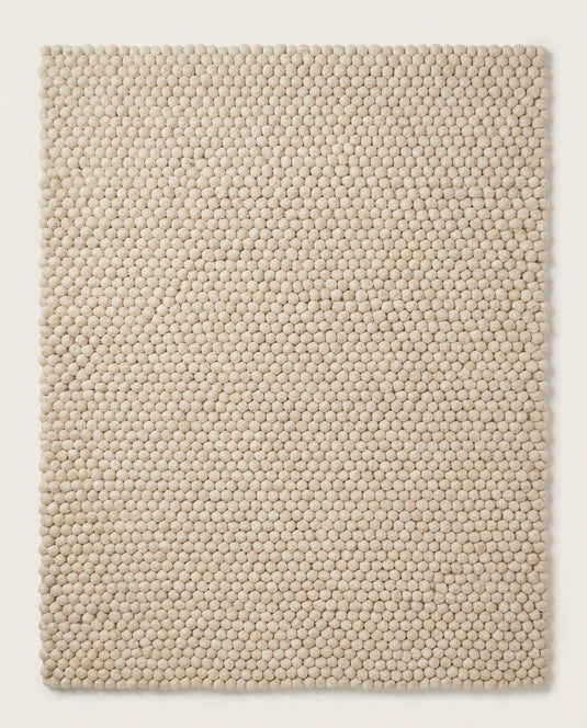 Translation missing: es.Handmade wool ball rug with chunky texture placed on wooden floor, perfect for boho nursery or minimalist bedroom