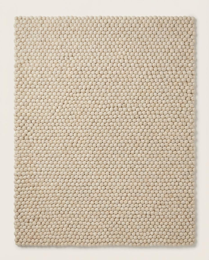Translation missing: es.Handmade wool ball rug with chunky texture placed on wooden floor, perfect for boho nursery or minimalist bedroom