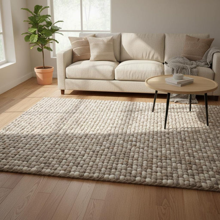 Translation missing: es.Handwoven chunky wool rug in neutral cream and beige tones with thick felted texture laying on wooden floor