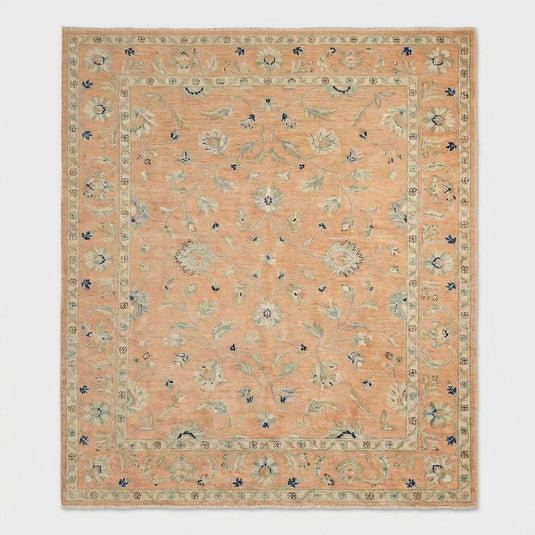 Translation missing: es.Angled view of pastel peach wool rug on light wood floor with velvet armchair showing interior design placement
