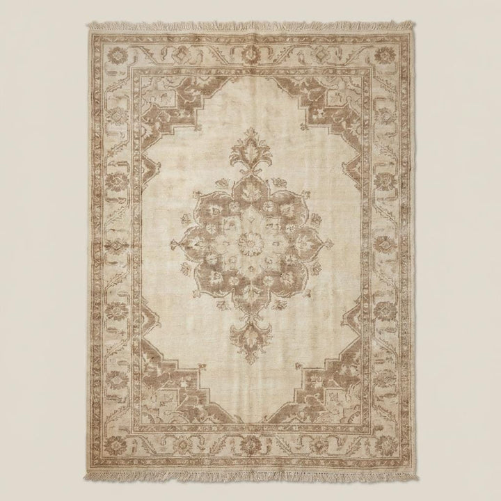 Translation missing: en.Traditional neutral beige handmade wool area rug with floral border and central medallion placed on dark wooden floor