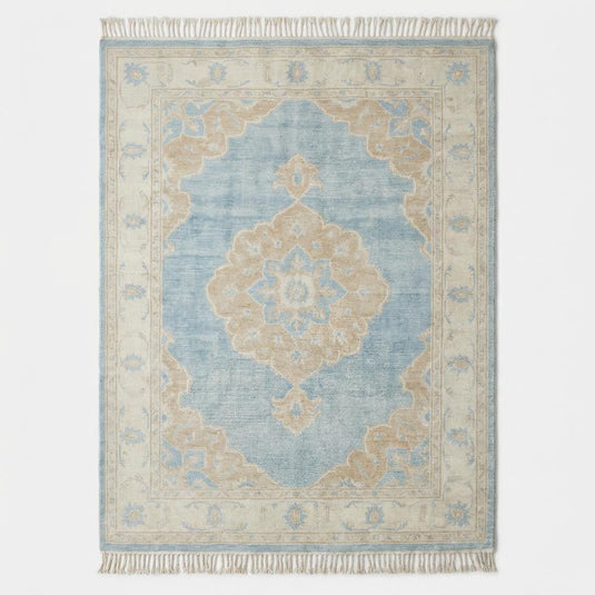Translation missing: es.Large blue wool area rug with ivory border and floral medallion placed on light wood flooring beside modern curved sofa