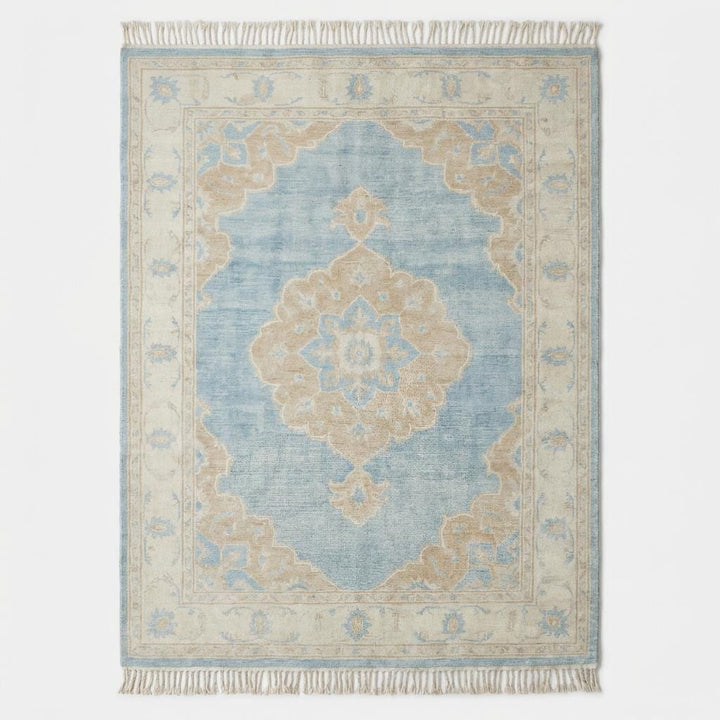 Translation missing: es.Large blue wool area rug with ivory border and floral medallion placed on light wood flooring beside modern curved sofa