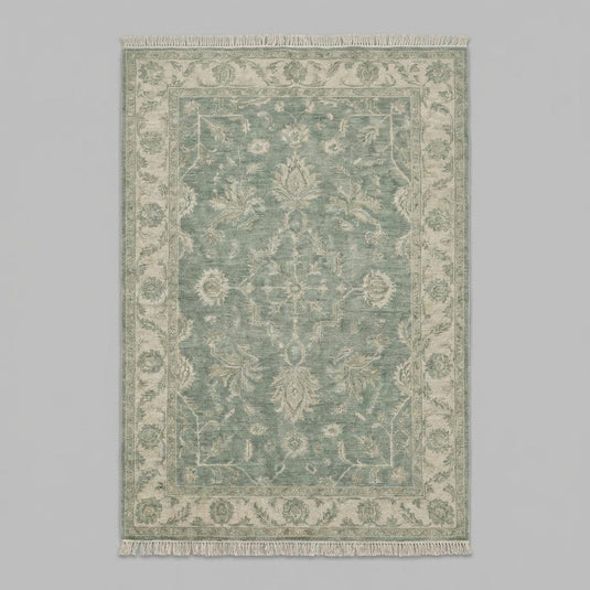 Translation missing: fr.Traditional green Oushak area rug styled on warm wooden floor beside soft linen chair and natural décor