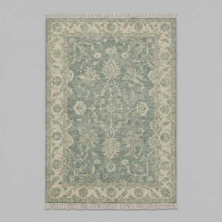 Translation missing: en.Traditional green Oushak area rug styled on warm wooden floor beside soft linen chair and natural décor
