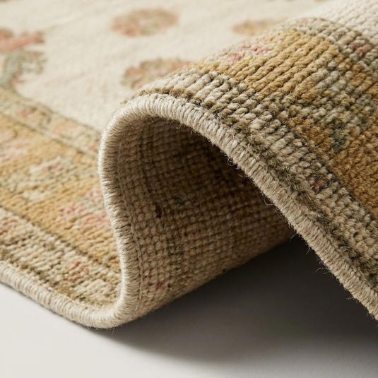 Translation missing: es.Close-up of hand knotted wool rug showing individual knot definition, dense wool pile, ivory base, and muted gold floral detailing with visible artisan weave structure