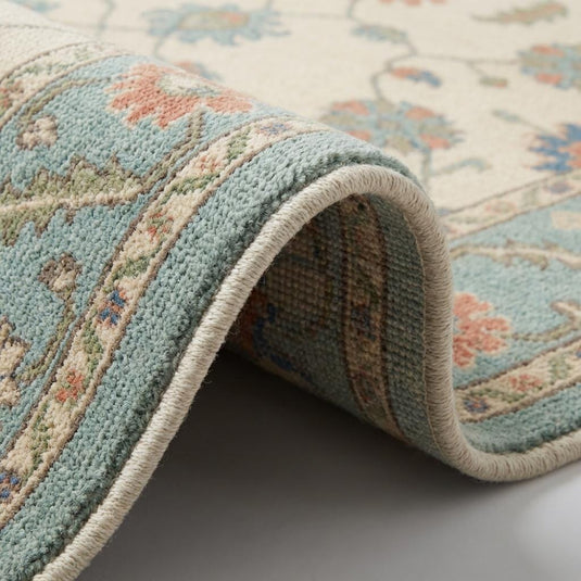 Translation missing: es.Close up of hand knotted wool pile showing individual knot structure, dense weave, and soft cream and teal floral detailing