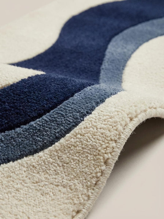 Translation missing: es.Close up of dense hand tufted wool pile showing soft cut-pile texture and carved wave pattern detailing in navy and slate blue fibers
