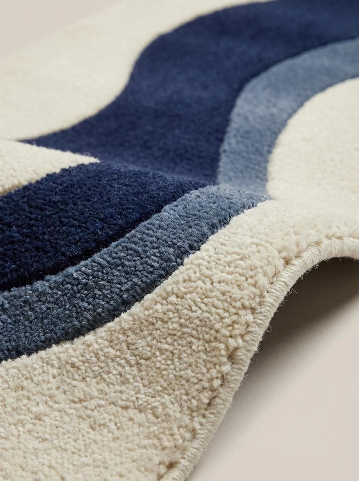 Translation missing: es.Close up of dense hand tufted wool pile showing soft cut-pile texture and carved wave pattern detailing in navy and slate blue fibers