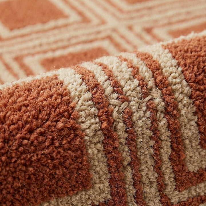 Translation missing: es.Close-up of hand tufted wool rug showing dense cut pile texture with carved high-low square pattern detailing in rust and cream tones