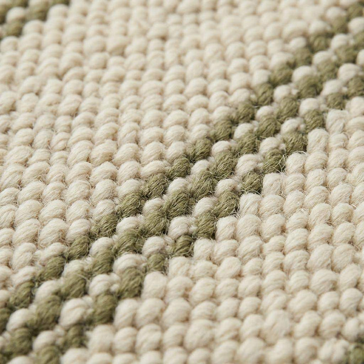 Translation missing: es.Close-up texture of thick wool fibers on a natural cream rug with sage green stripe accents