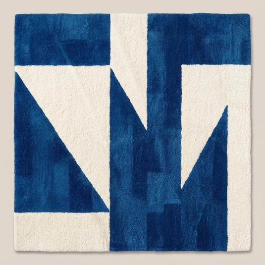 Translation missing: en.Contemporary blue geometric area rug with bold shapes placed in front of a wooden sofa in a sunlit interior space