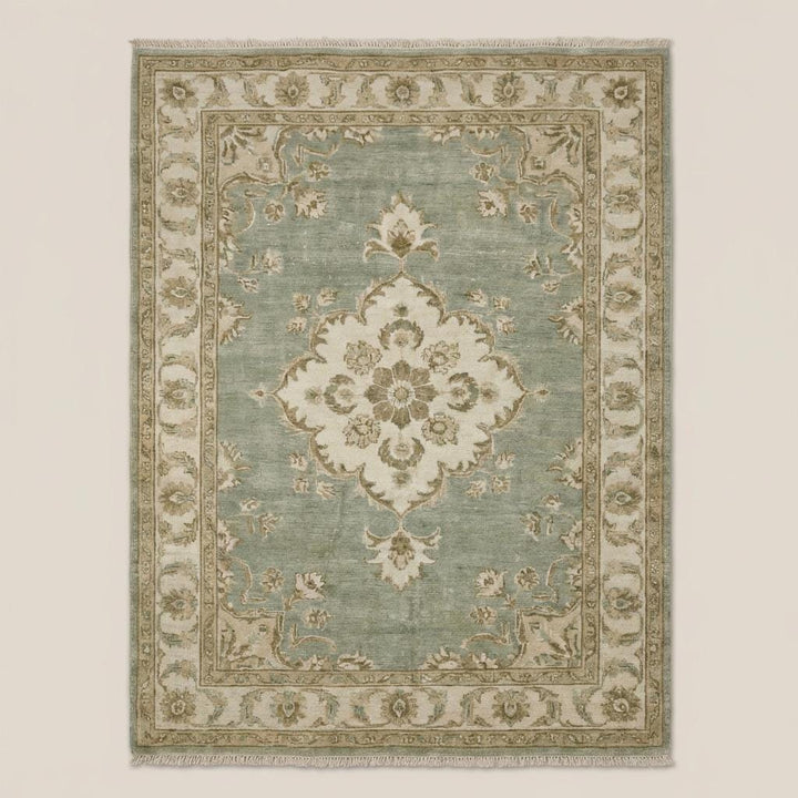 Translation missing: en.Traditional Oushak style floral medallion rug in sage green and beige tones on dark wooden flooring
