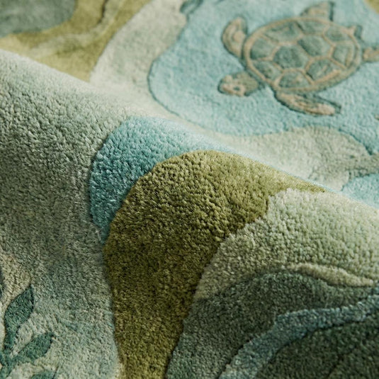 Translation missing: es.Close-up of tufted sea turtle rug texture showing carved wavy edges, plush fibers, and raised aquatic pattern in soft green and blue tones