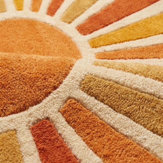 Translation missing: es.Close up texture of hand tufted wool rug showing dense plush cut pile with carved sunburst geometric pattern in rust orange and cream wool fibers