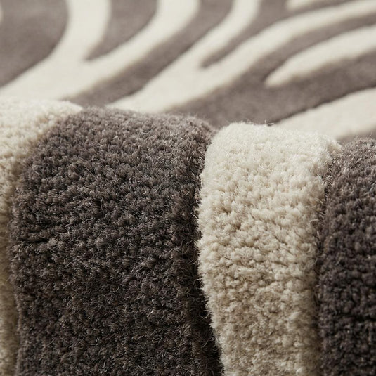 Translation missing: es.Close-up of hand tufted wool fibers showing raised carved zebra stripes, plush pile texture, and dense wool surface in ivory and charcoal tones