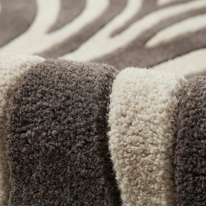 Translation missing: es.Close-up of hand tufted wool fibers showing raised carved zebra stripes, plush pile texture, and dense wool surface in ivory and charcoal tones