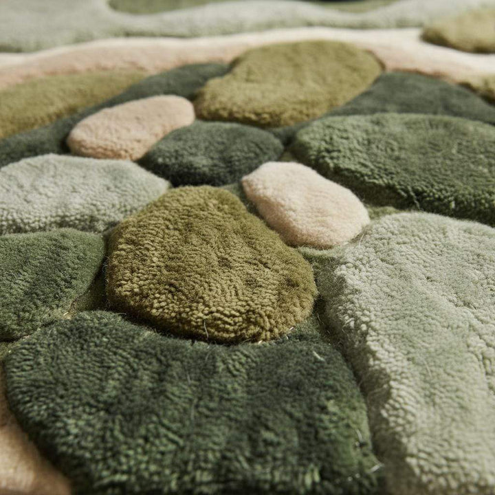 Translation missing: es.Close-up of hand tufted rug texture showing high and low pile fibers, soft plush material, and sculpted abstract pattern in green and beige tones highlighting craftsmanship and premium quality